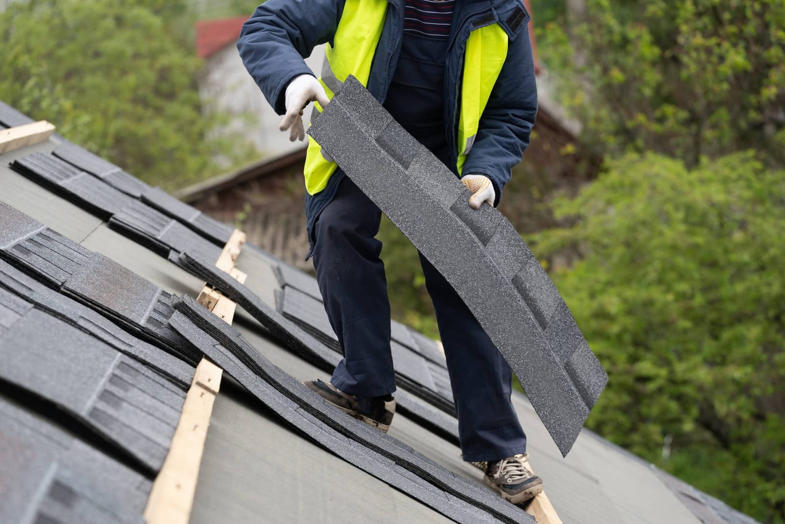 Roofer carrying a bundle of asphalt shingles across a roof under repair